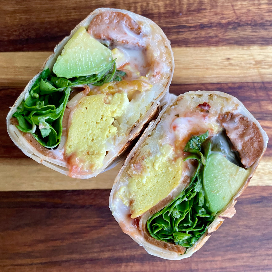 Vegan breakfast burrito cut in half, showing scrambled tofu, greens and avocado